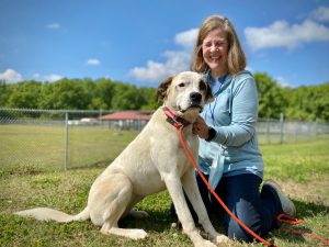 A Huntsville Animal Services volunteer poses for a photo with a mixed-breed dog on a sunny day.