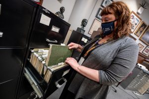 Archivist Shalis Worthy takes a green folder from a black filing cabinet at the the Huntsville-Madison County Public Library Special Collections Department