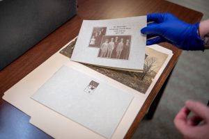 Archivist Shalis Worthy, wearing a blue glove, flips through historic photos in a folder at the HMCPL Special Collections Department