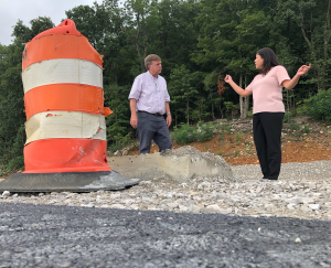 Mayor Tommy Battle and Engineering Director Kathy Martin talk next to a road pylon. There is gravel in the foreground and trees in the background.