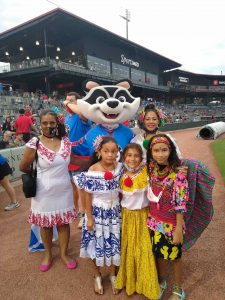 Flora E. Tapia-Johnson, left, participates in a Hispanic Heritage Month event at Toyota Field in Madison in September 2020. The trash panda mascot is present as are some girls in colorful garb.