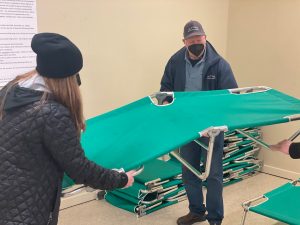 A woman and a man unfold a green cot at a temporary warming shelter.