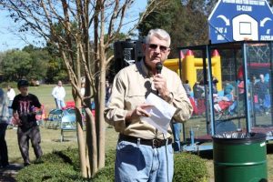 Lyle Voyles speaks into a microphone to a crowd gathered at a neighborhood picnic.