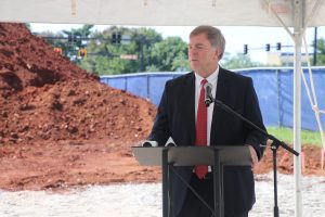 Mayor Tommy Battle speaks at a 2022 groundbreaking ceremony for Vista at Councill Square. He is wearing a black suit and there is a large mound of dirt in the background.