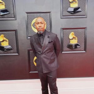 Producer Kelvin Wooten is seen at the Grammy awards. He is wearing a dark purple suit.