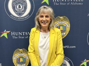 Cindy Green, an Administrative Aide with the Huntsville Police Department, poses in front a large blue poster with the Huntsville Police logo on it.