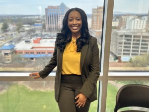 KeAirra Green, the City of Huntsville's Equal Employment Opportunity Officer, stands in front of a large window over the the downtown area.