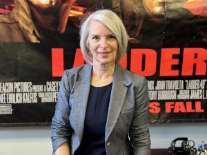 Lesley Easter, the Support Services Manager at Huntsville Fire & Rescue, smiles in front of a giant poster of the movie "Ladder" in her office.