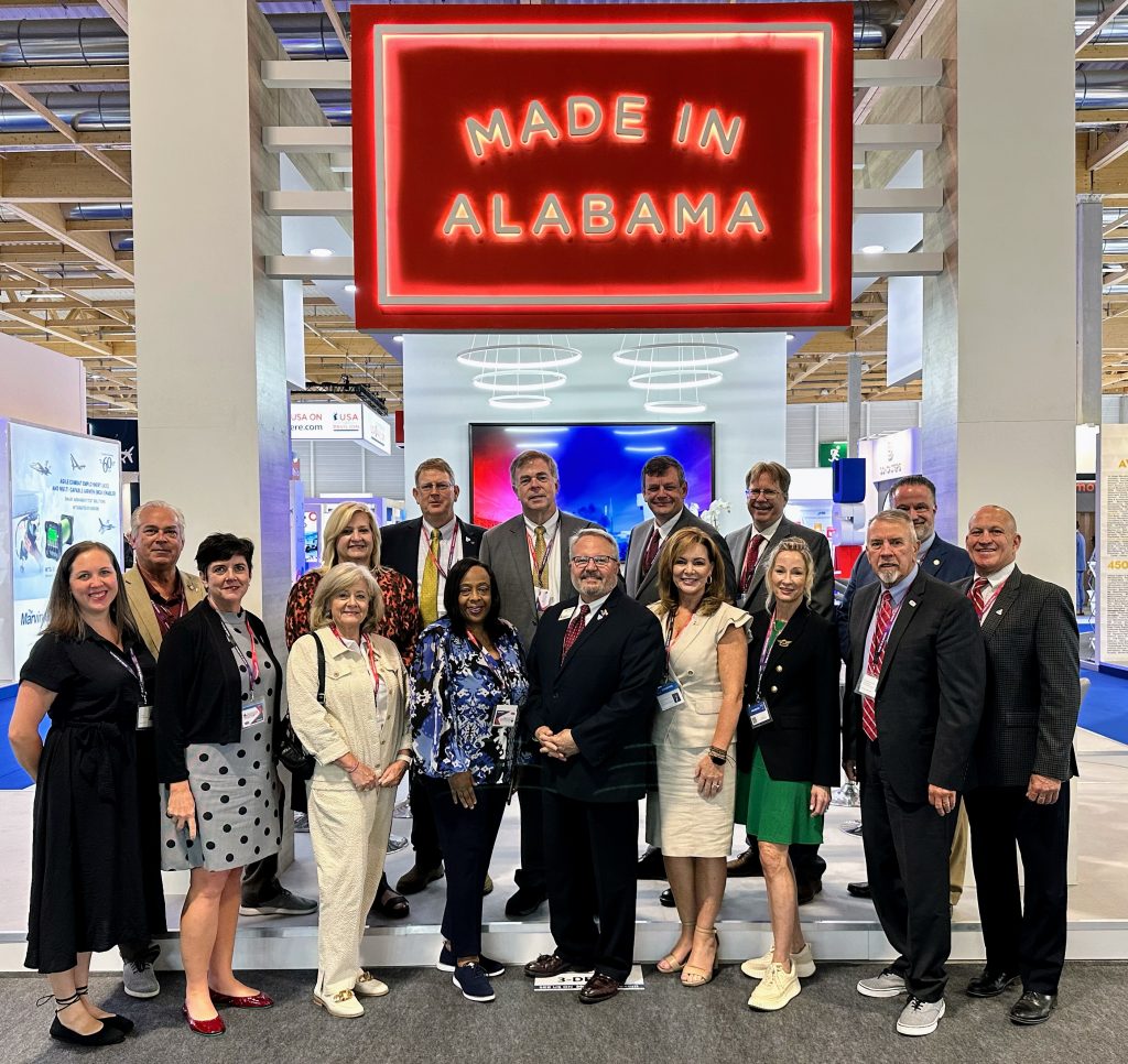 group of people standing in front of a red Made in Alabama sign at the state's booth at the Paris Air Show