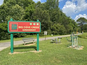 A sign reading "Big Cove Creek Greenway" next to a paved pathway.