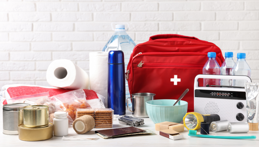 A photo of emergency supplies on a counter, including first aid kit, food, water, and a radio.