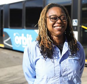 Huntsville Transit bus operator Kisha Ballard stands next to an Orbit fixed-route bus.