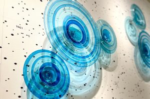 An art installation of blue glass disks on a white wall of constellations.