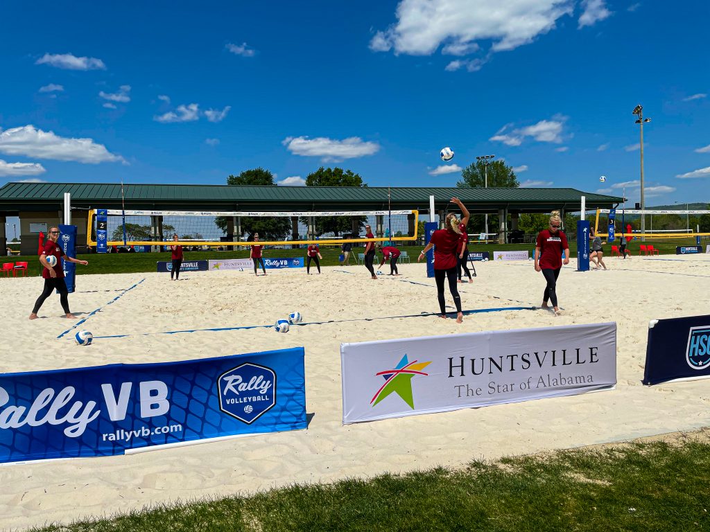 college volleyball team practicing on sand court beneath blue sky