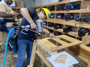 Photo of a female student in hard hat using a pneumatic nailer at the North Alabama Home Building Academy