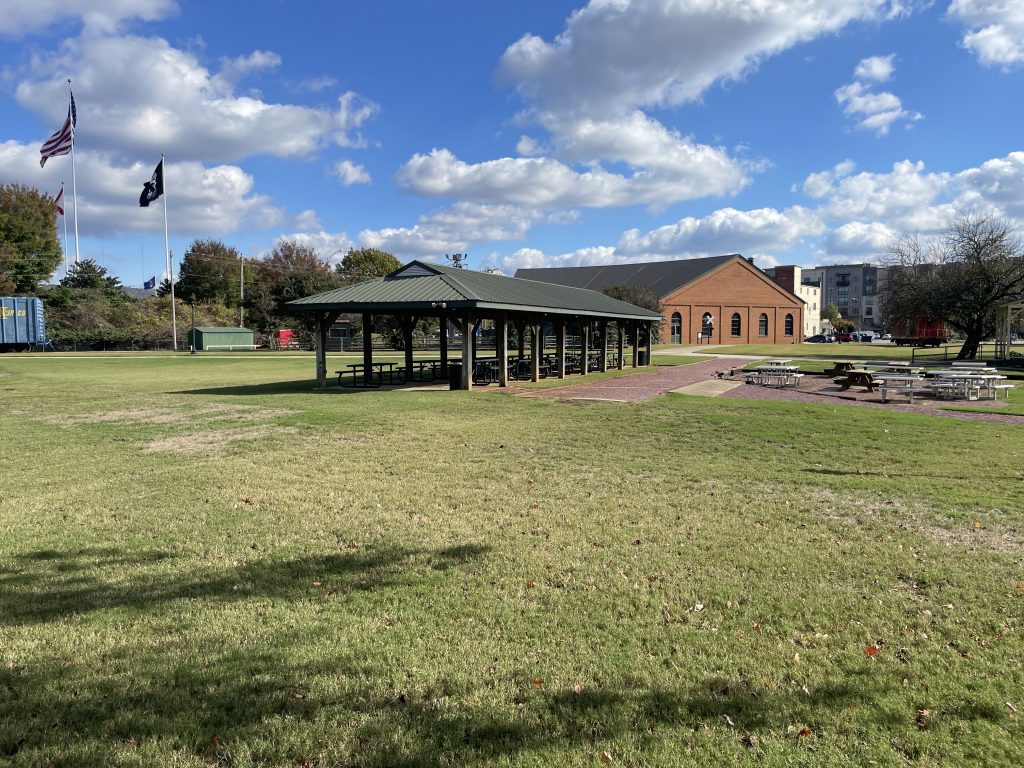 grass field with pavilion and brick building and blue sky in background