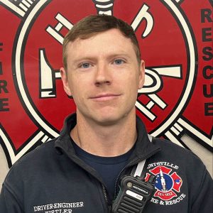 man in dark shirt with fire department logo on left shoulder with red background