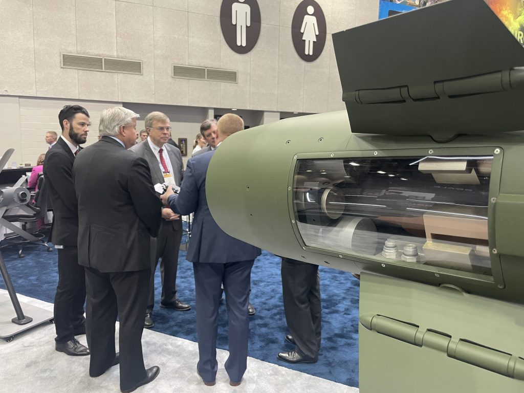 group of people standing in conversation with tail end of green missile in foregrond