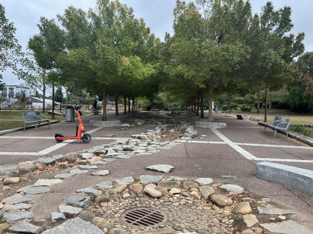 An orange electric scooter sits at left on Atlanta's Beltline, There are also trees and benches visible.