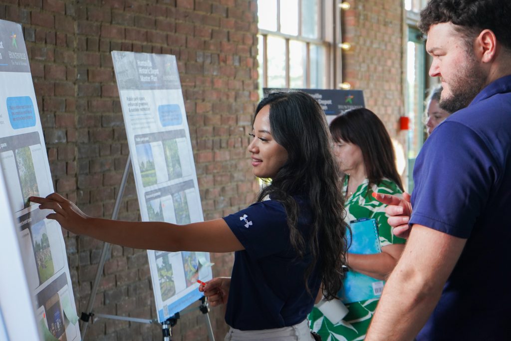woman and man wearing blue shirts looking at poster display in front of brick wall